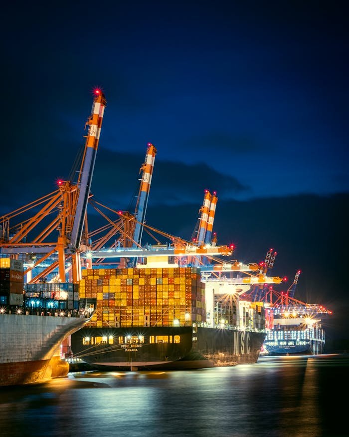 our-services-02 Vibrant night view of container ships at Hamburg port with cranes illuminated.