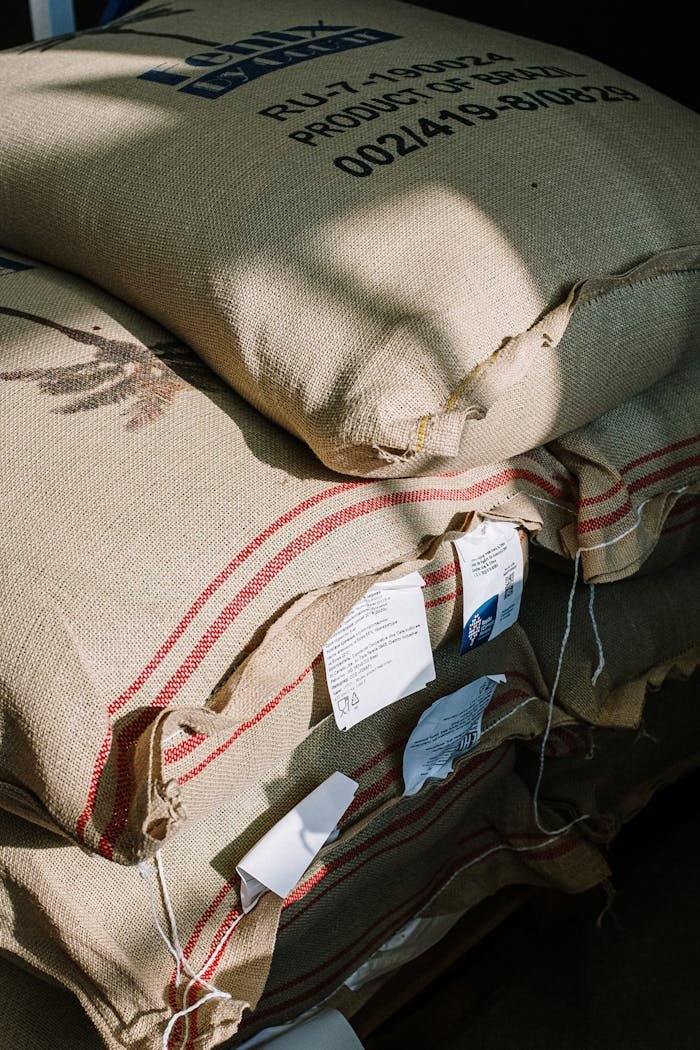 our-services-01 Stack of burlap sacks filled with organic coffee beans in a roastery, captured with natural light.